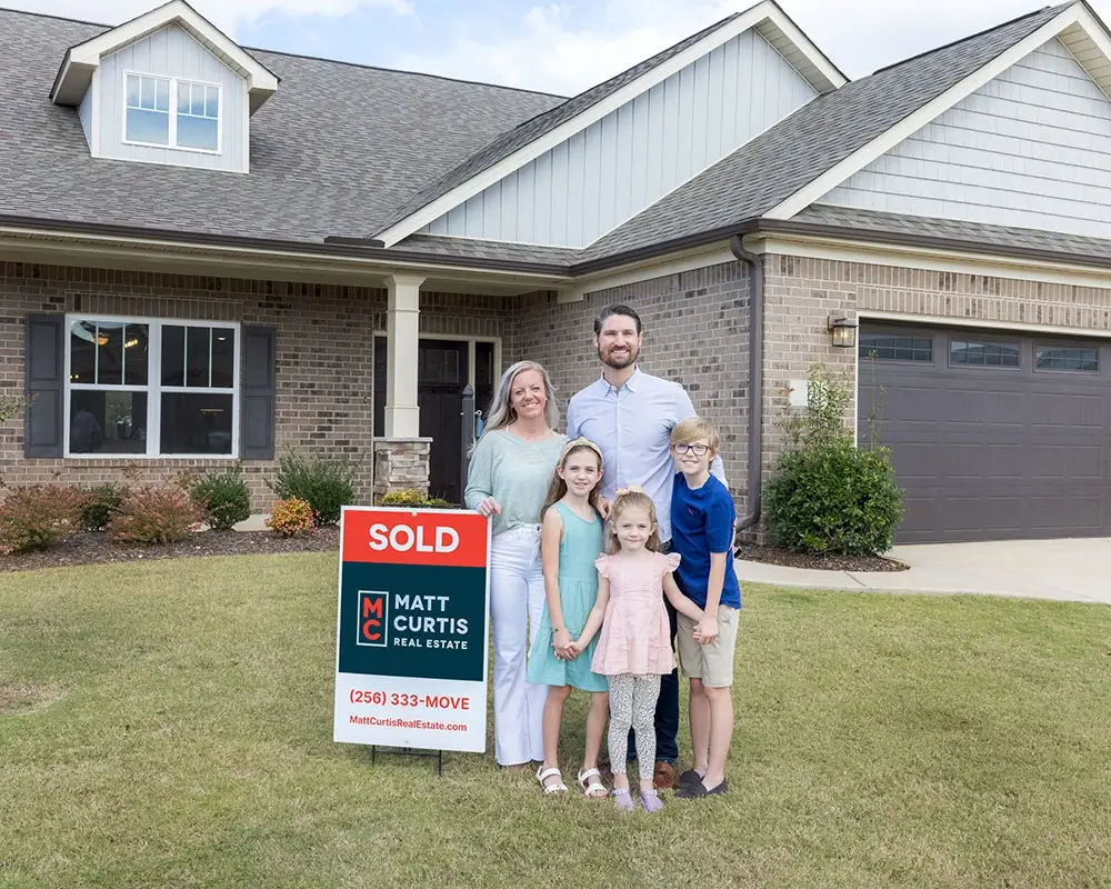 Happy family standing beside a Matt Curtis SOLD sign